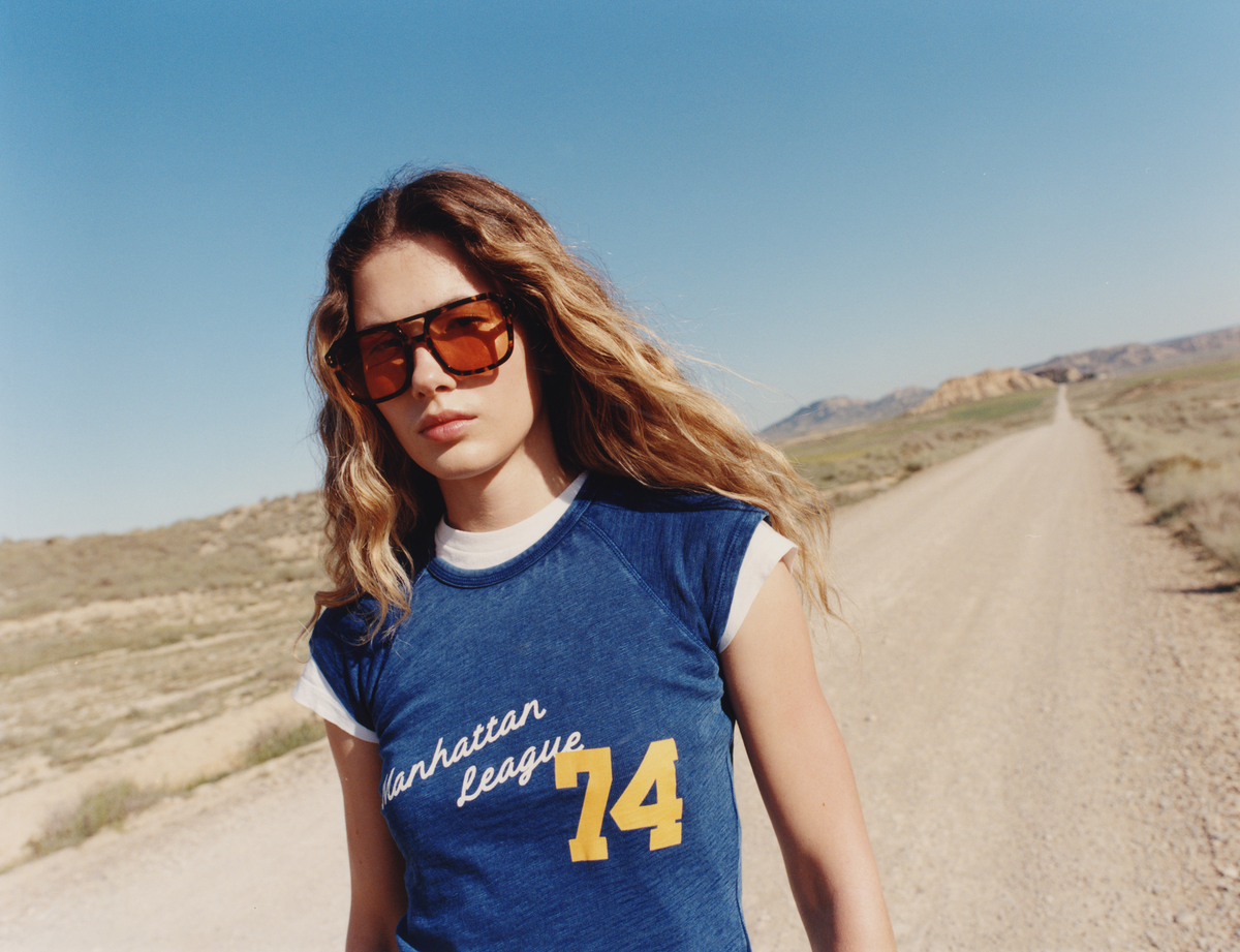 Woman wearing a blue t-shirt with 'Manhattan League 74' on a desert road.